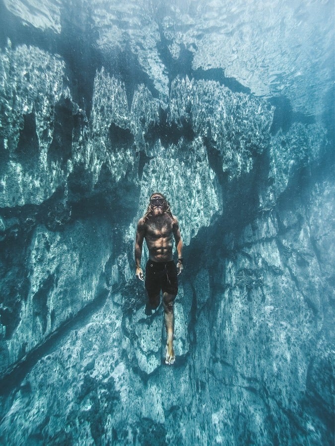 a man is swimming in the water near rocks.