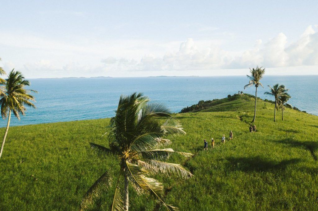 a group of people walking on a grassy hill next to the ocean.
