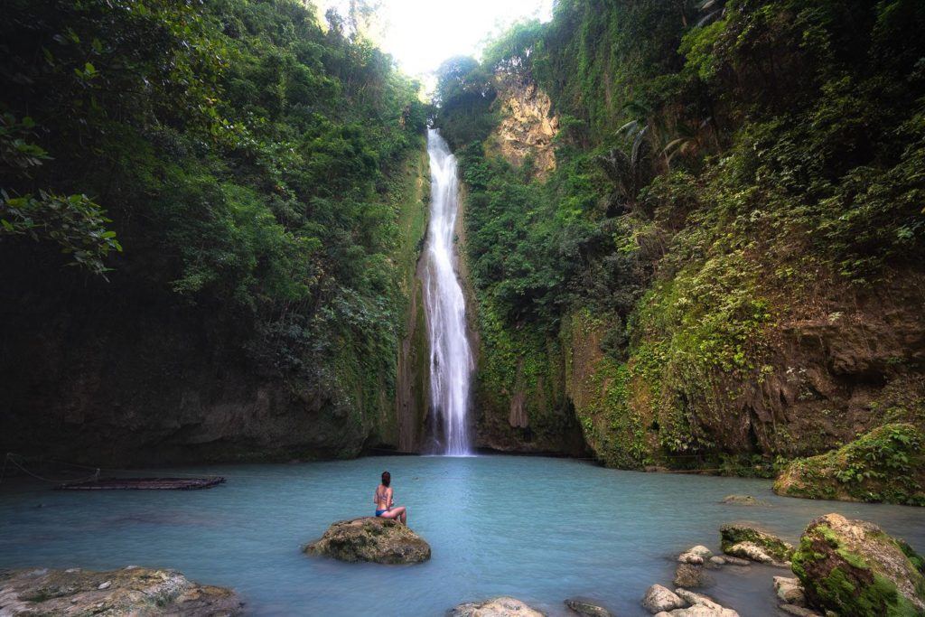 a person sitting on a rock in front of a waterfall.