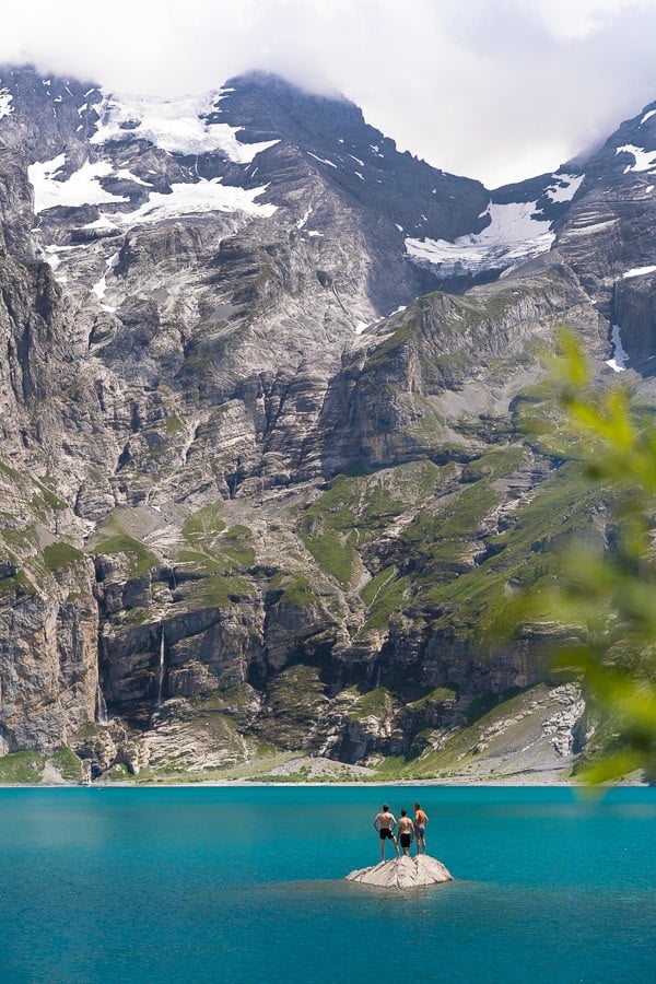 a couple of people standing on top of a rock in the middle of a lake.