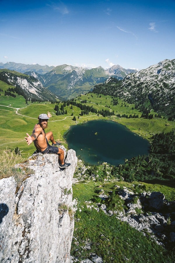 a man sitting on top of a rock next to a lake.