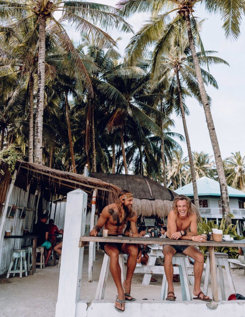 two women sitting at a table in front of palm trees.