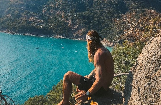 a man sitting on top of a rock next to a body of water.