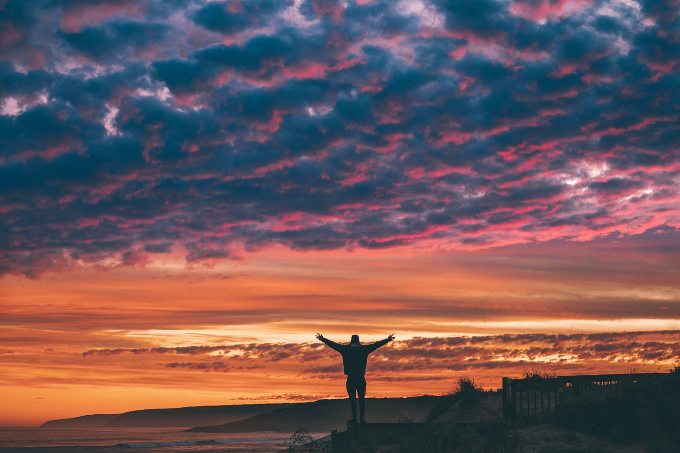 a person standing on top of a cliff at sunset.